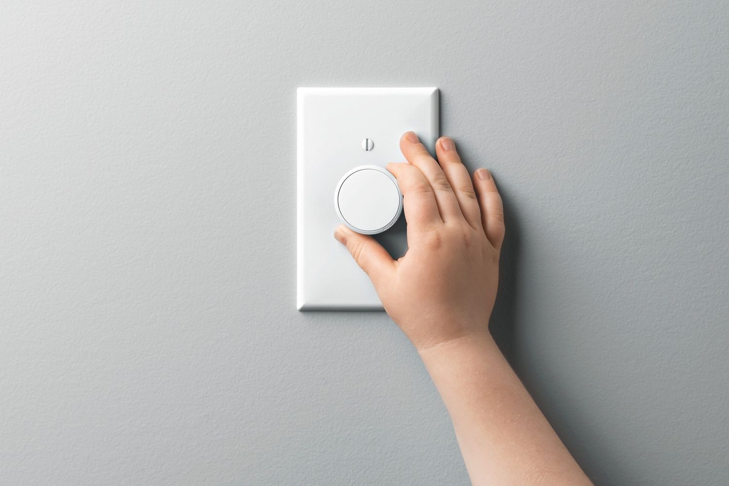 A hand turning the dial on a light dimmer switch.