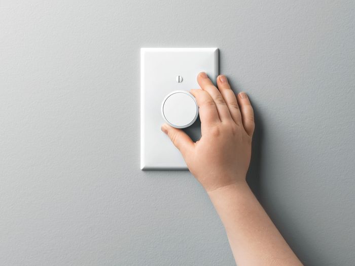 A hand turning the dial on a light dimmer switch.