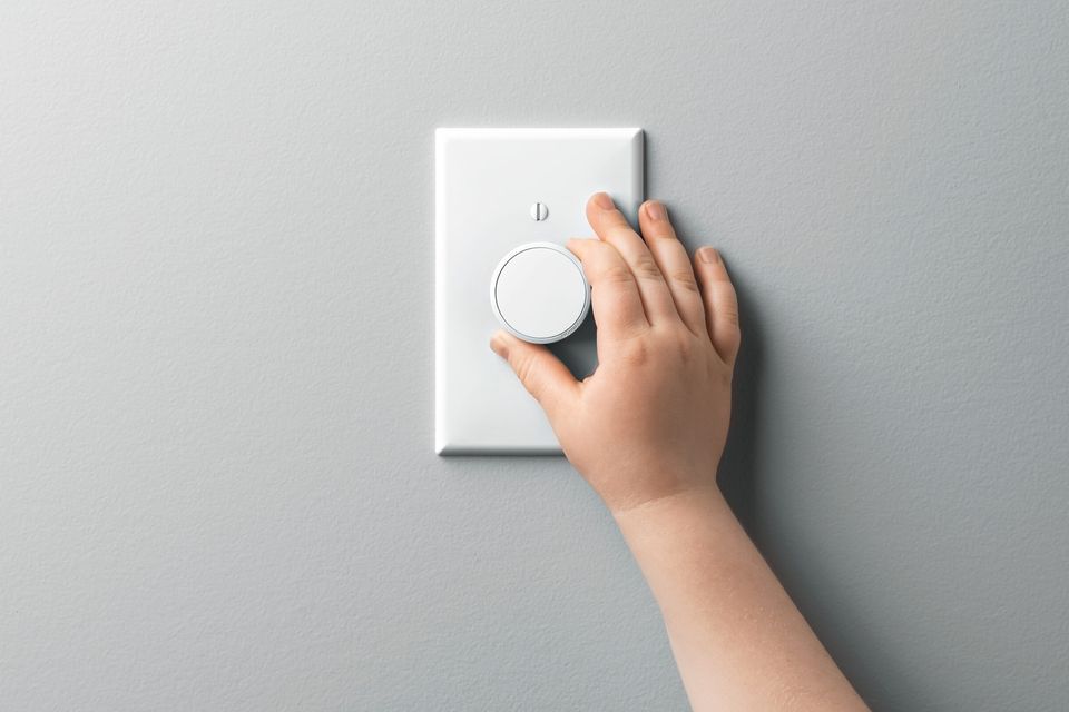 A hand turning the dial on a light dimmer switch.