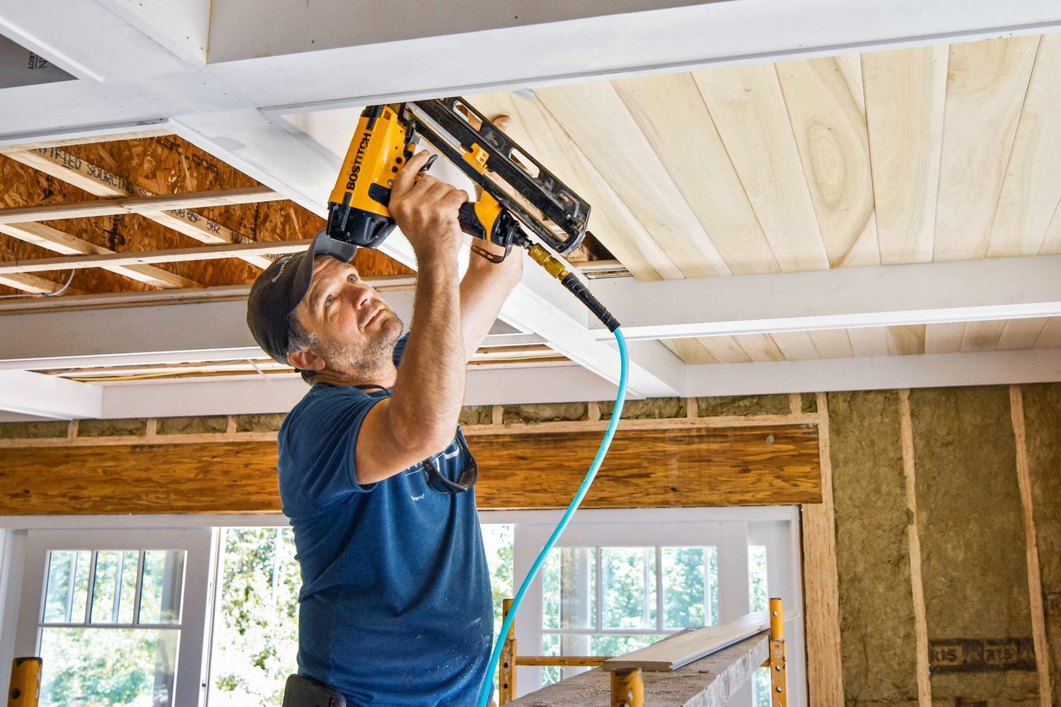A man using a nail gun to work on replacing a ceiling.