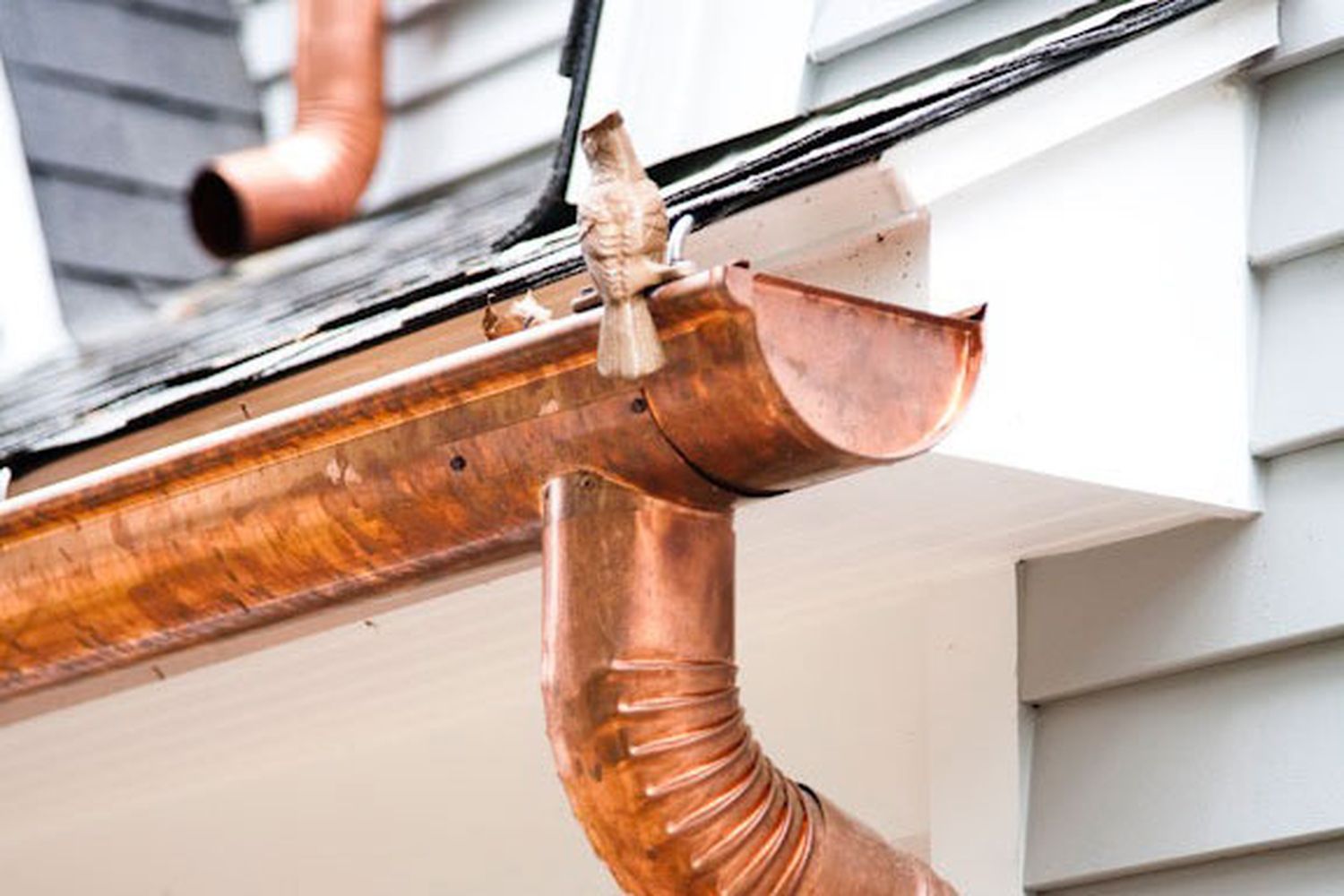 A copper gutter with a downspout attached to the side of a home.