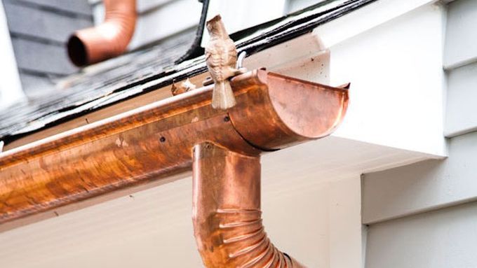 A copper gutter with a downspout attached to the side of a home.