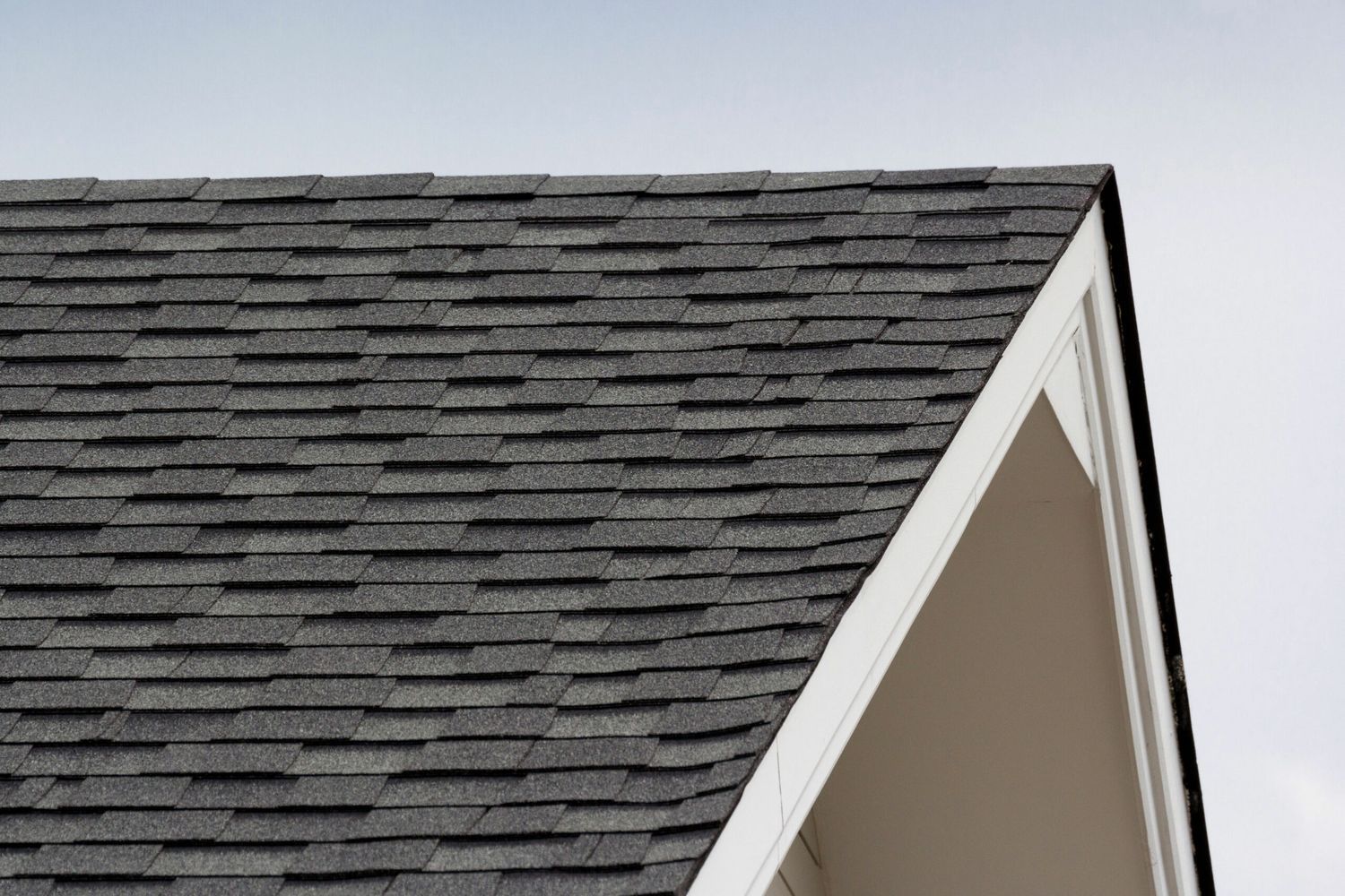 A triangular roof with black shingles on a white trusses