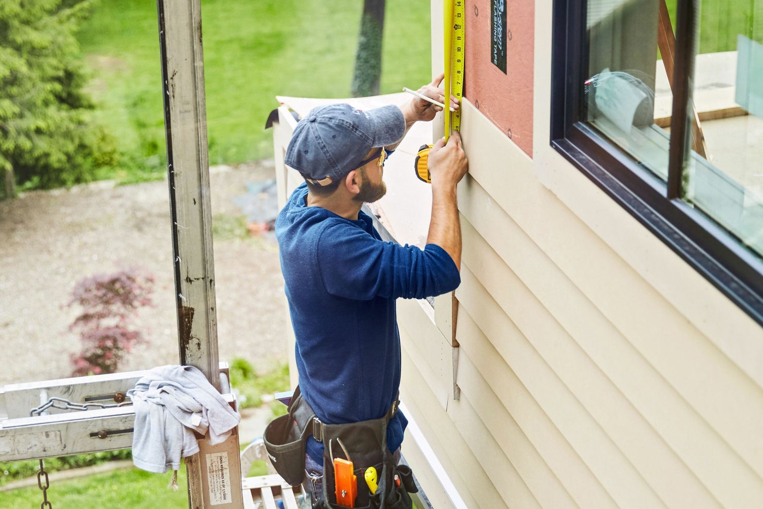A man using a tape measure to measure the siding of a house.