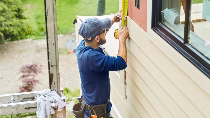 A man using a tape measure to measure the siding of a house.