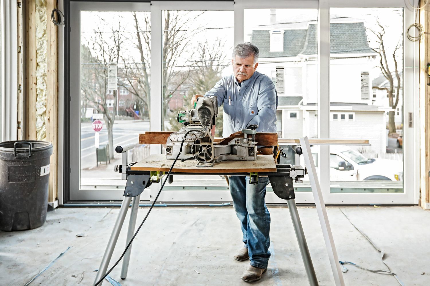 A man working at a table in front of a window with several hand and power tools.