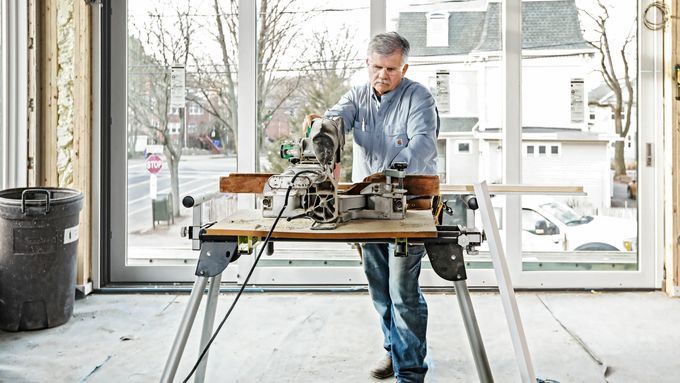 A man working at a table in front of a window with several hand and power tools.