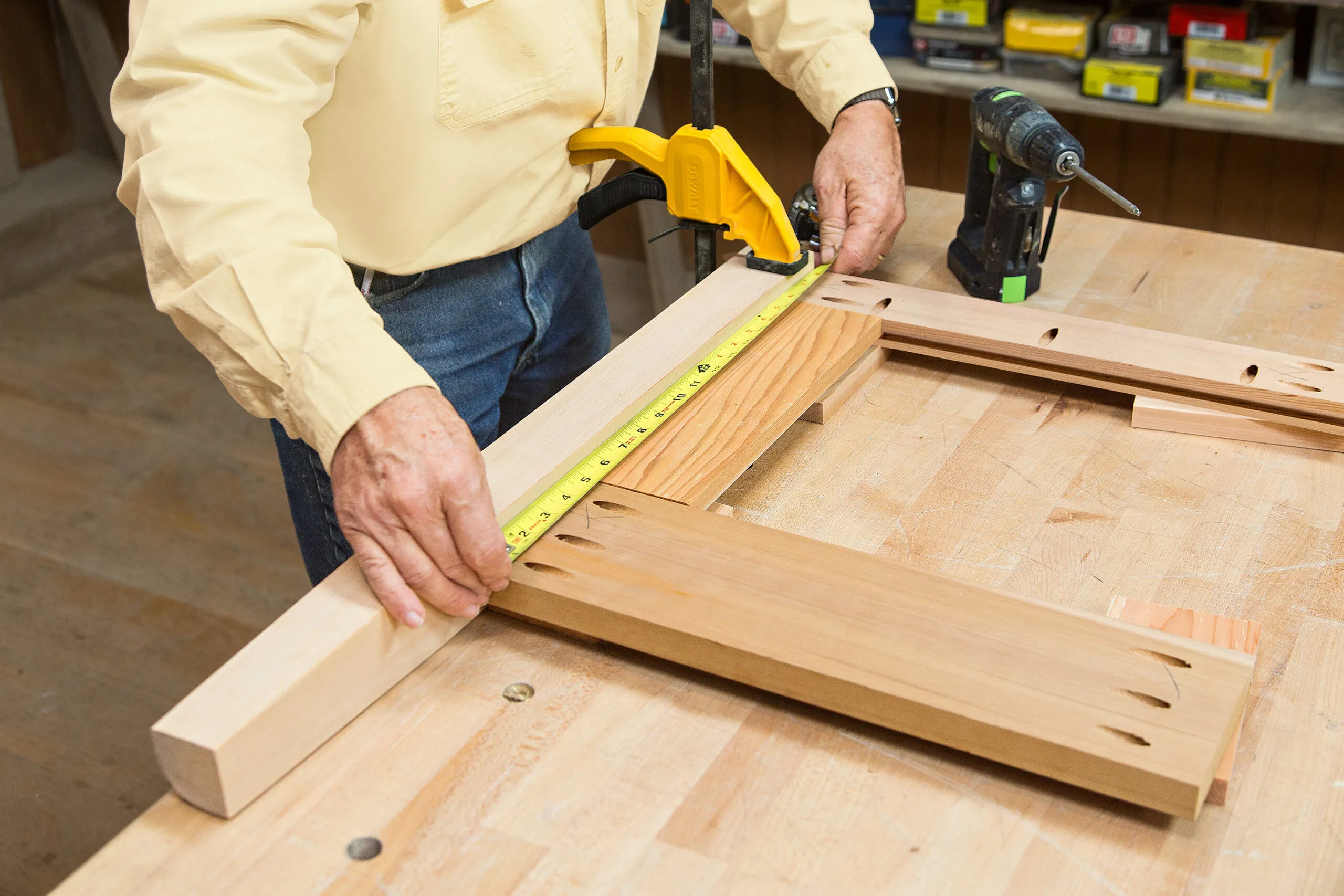 A person measures the bottom rail of a cedar planter box with a measuring tape.