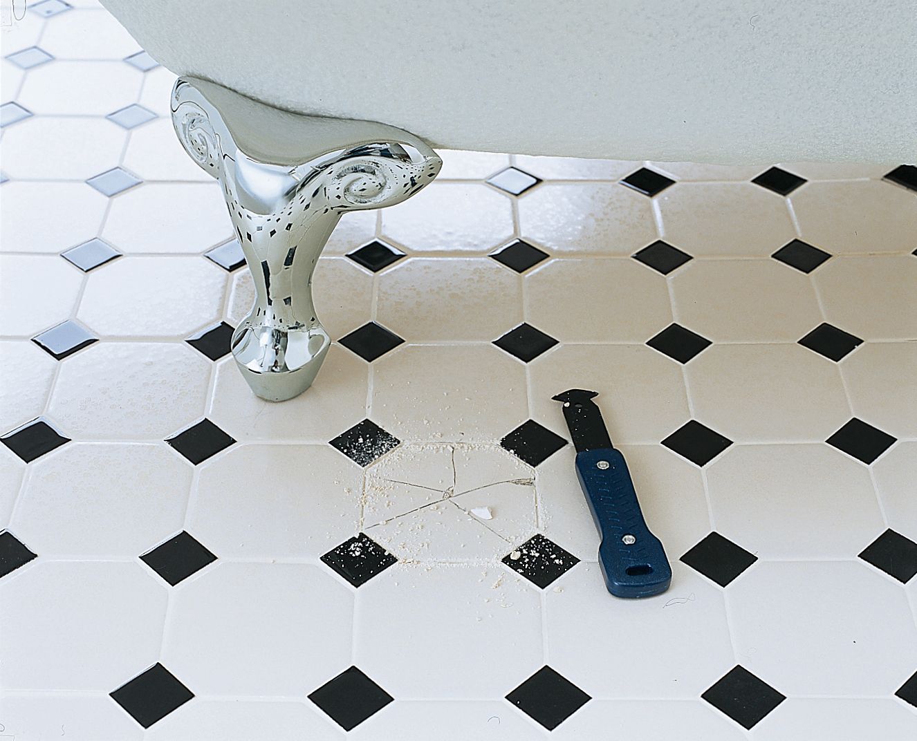 A bathroom floor with a cracked tile beside the foot of a bathtub.