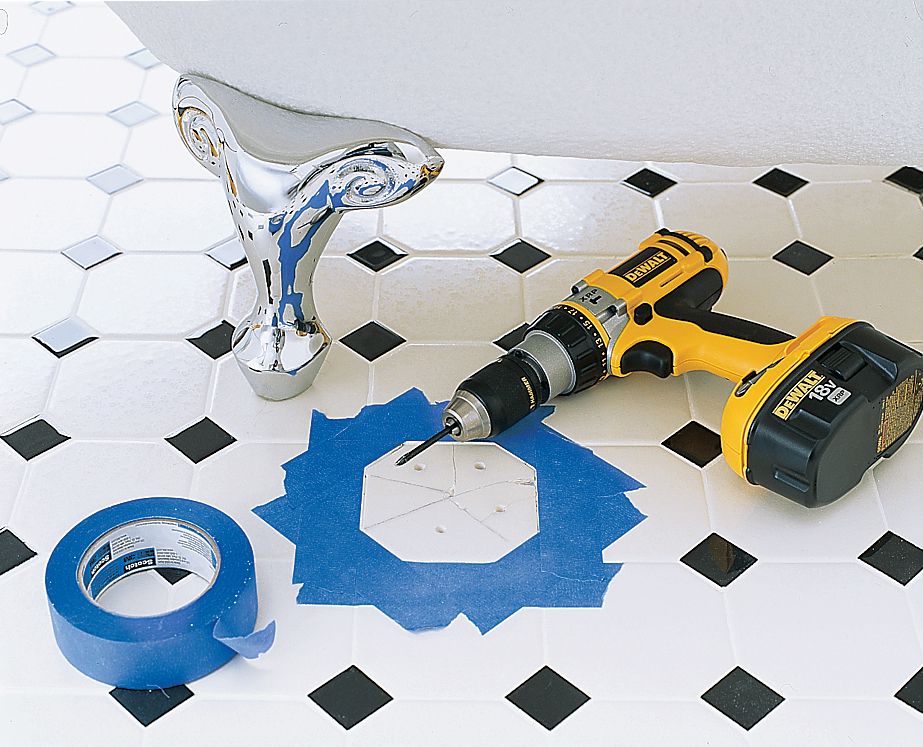 A broken tile in a bathroom that has been marked off with blue tape. A drill sits beside the broken tile.