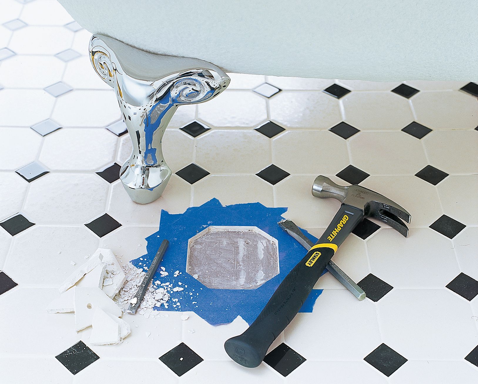 A bathroom with a broken tile removed from it's center. The fragments of the tile are piled on the left side of the image and a hammer and chisel sit on the right side.