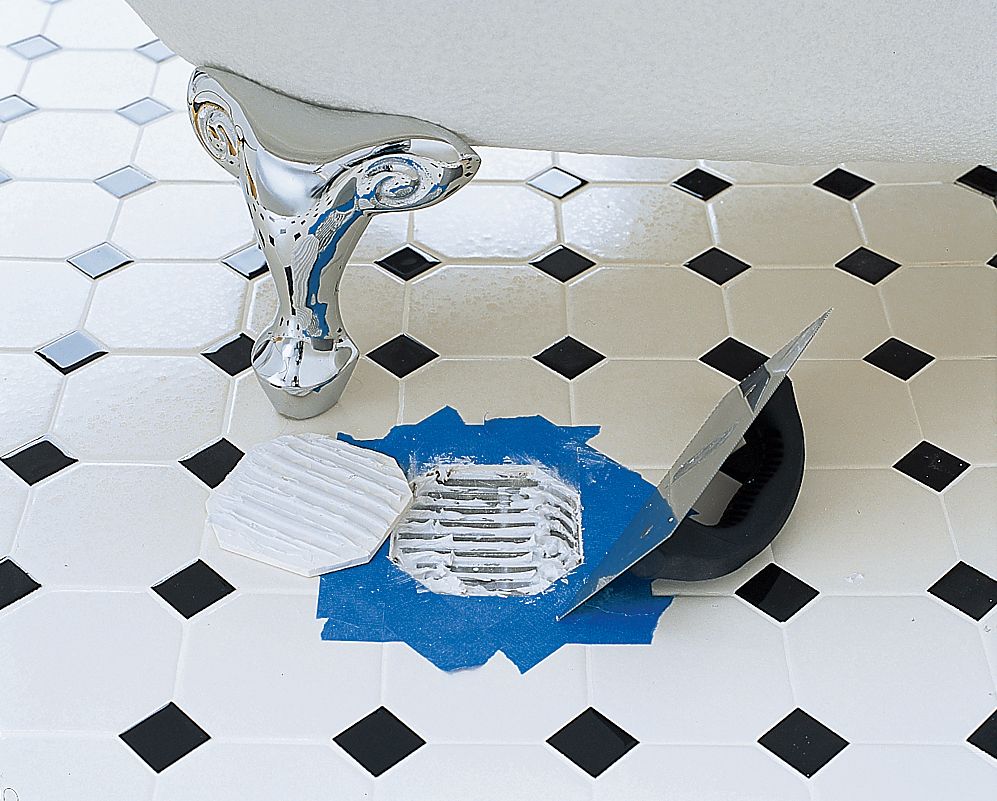 A bathroom floor with missing tile, a new, loose tile sits to the left of the missing tile with adhesive applied to it. 