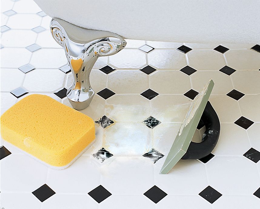 A bathroom floor with a new tile installed, a sponge a sits to the left of the new tile.