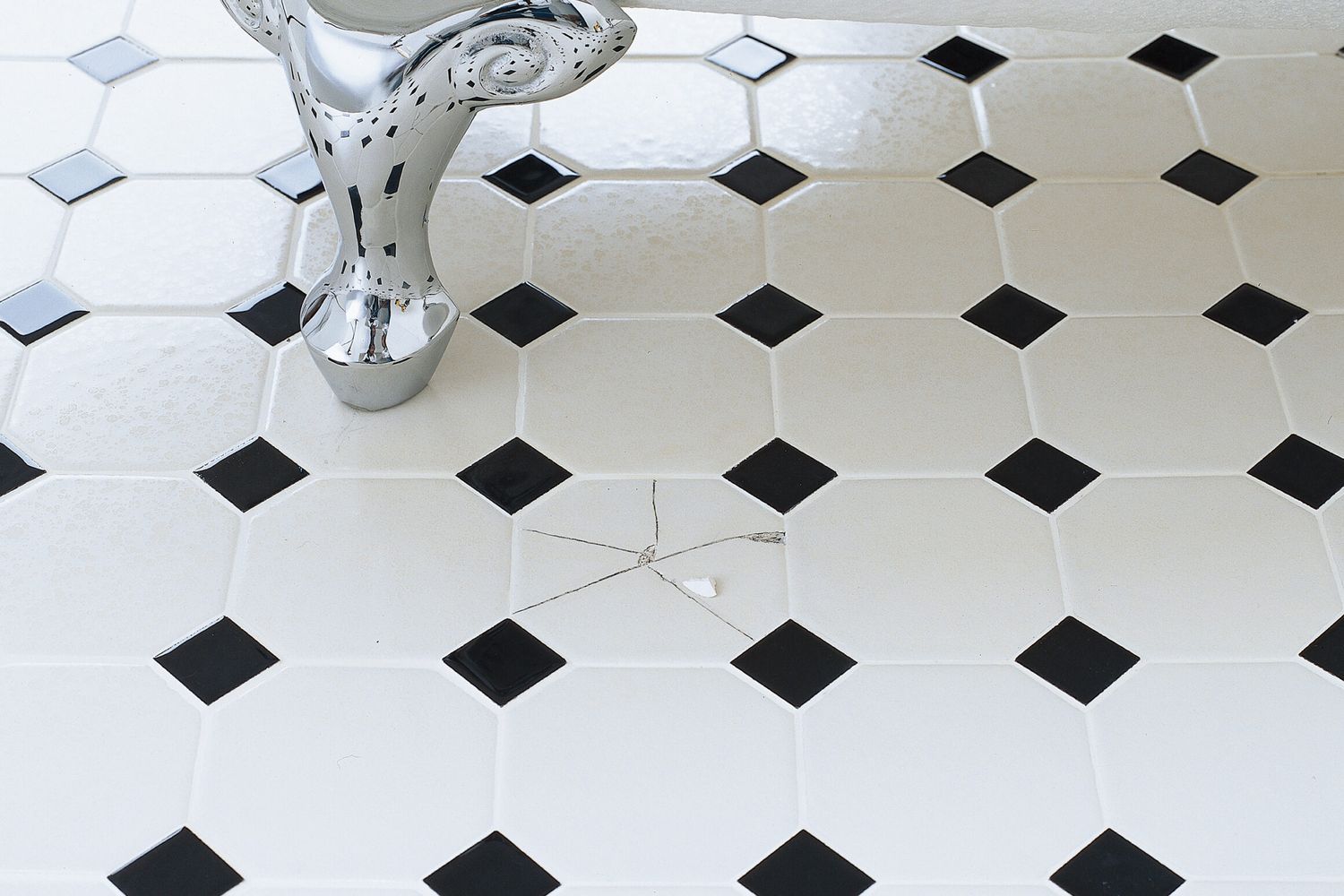 A bathroom floor with a broken tile beside a bathtub.