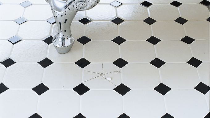 A bathroom floor with a broken tile beside a bathtub.