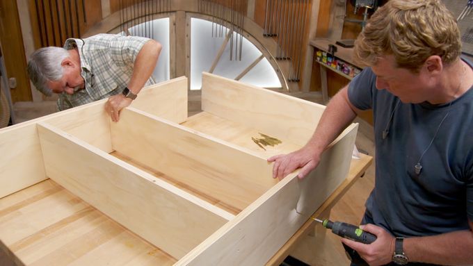 two people working on building a wooden bookshelf.