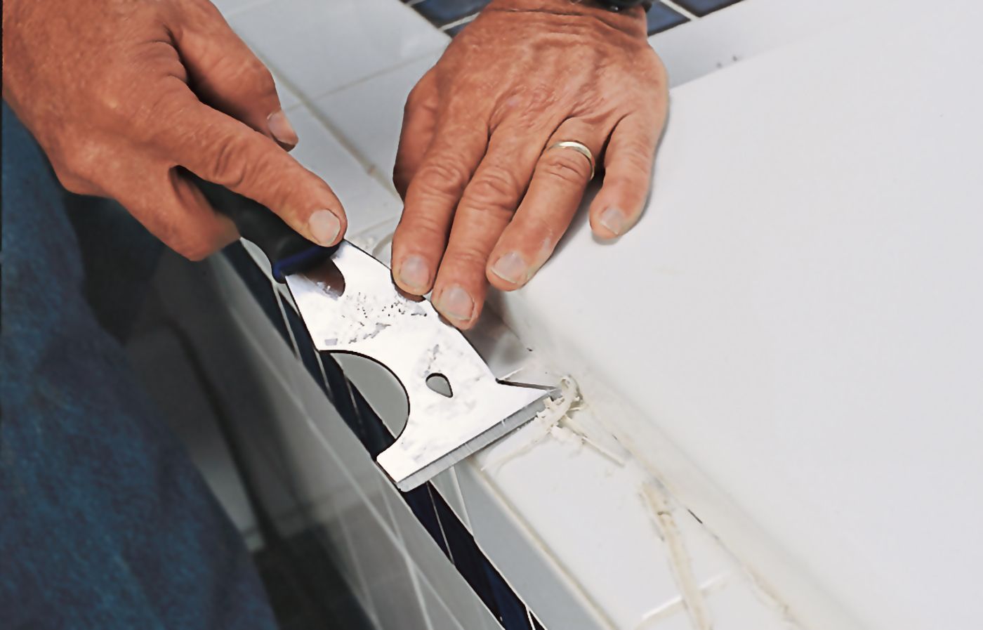 A person uses  scraper to remove old bathtub caulk.