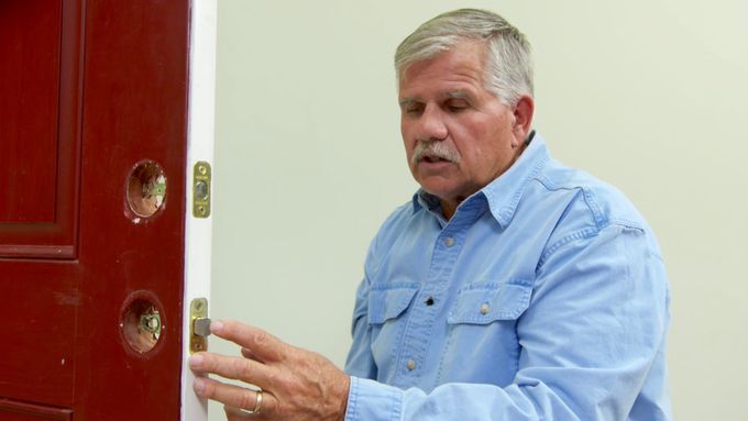 A man working on changing the locks of a red door.