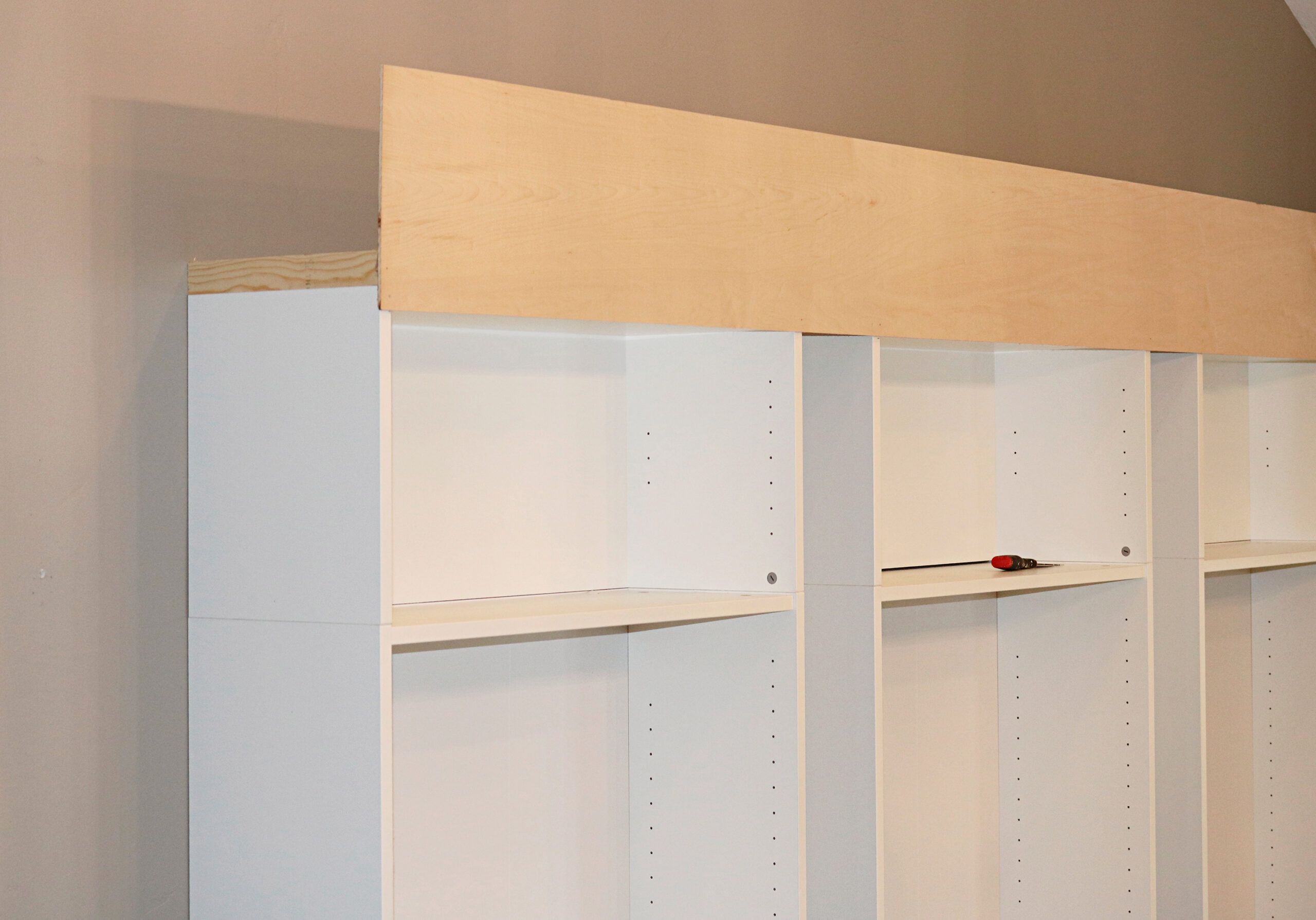 Three Ikea bookcases attached at the top by a piece of wooden strip to help give them the appearance of a built-in bookcase.