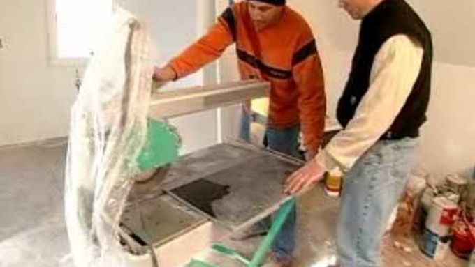 Two men preparing to cut through a piece of stone tile.