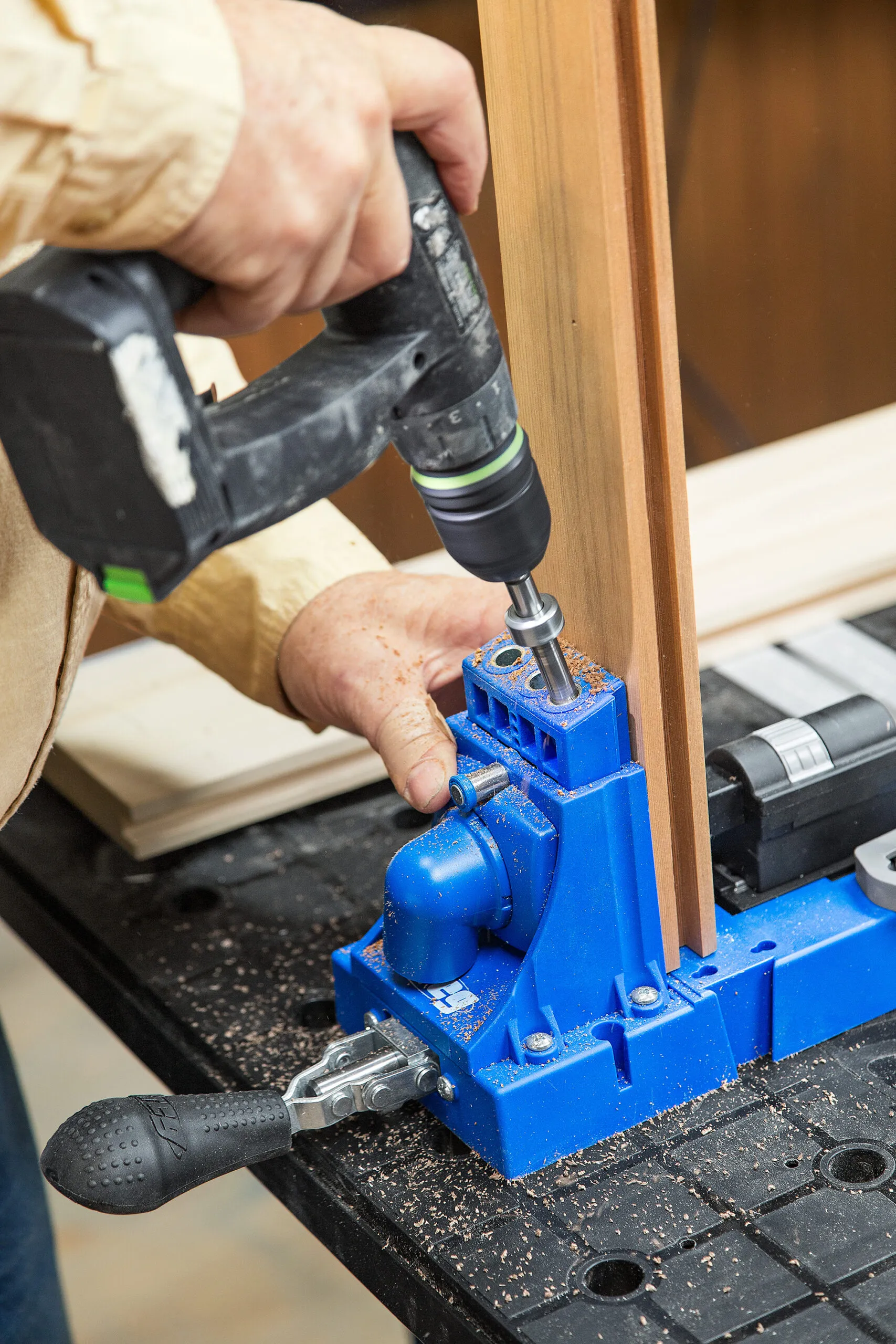 A person uses a pocket-hole jig and bit to drill holes in the cedar planter box rails.