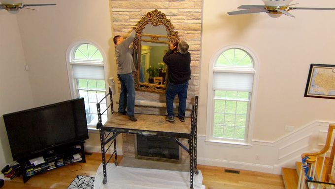 Two men hanging a mirror on a masonry surface.