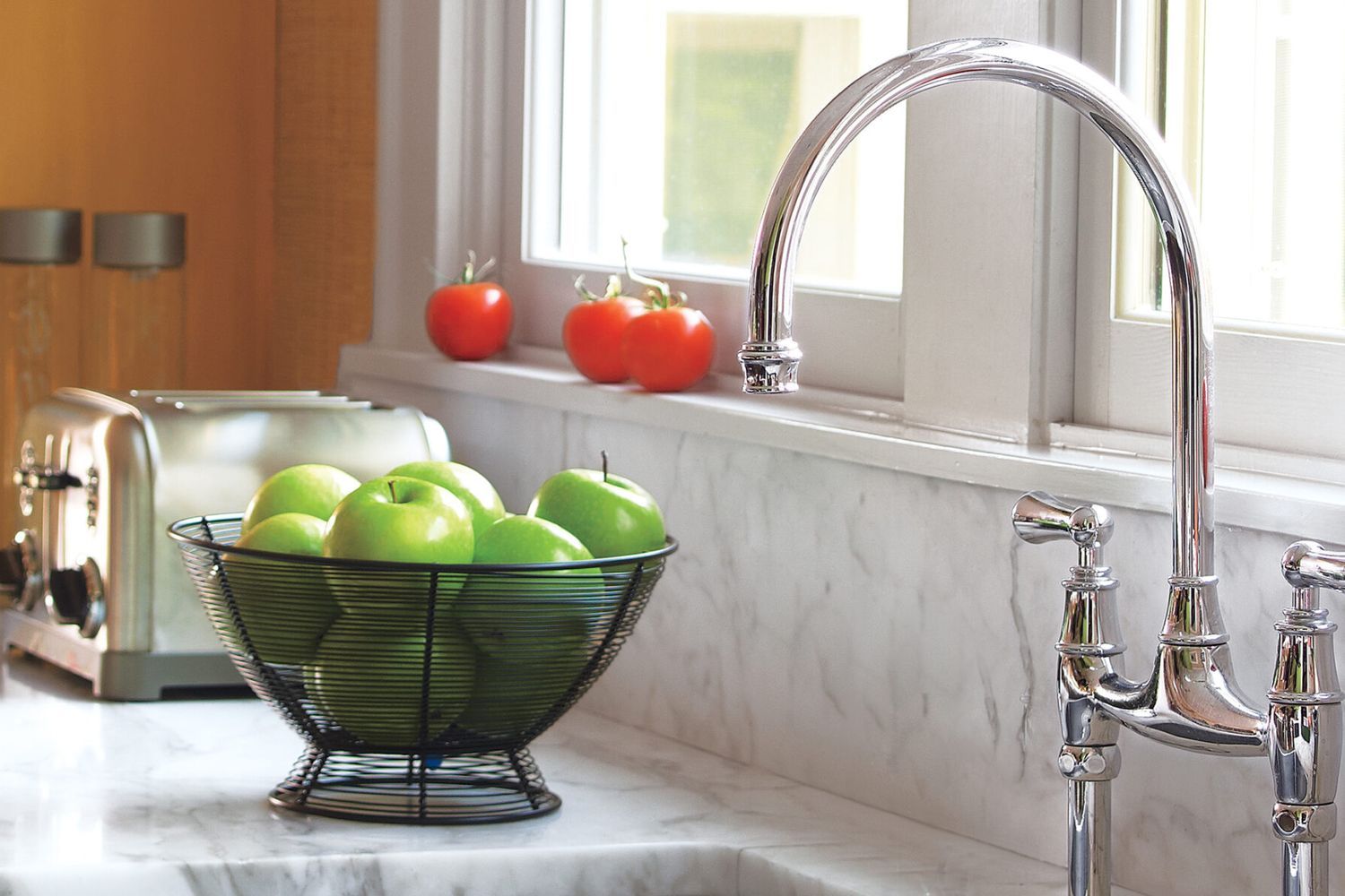 A stainless steel kitchen faucet by a bowl of apples.