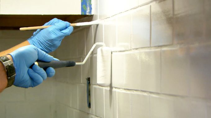 A man painting a tile backsplash with a roller and a brush.