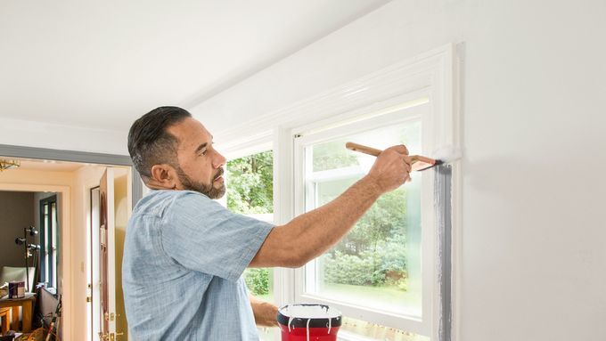 A man painting the edges of a window.