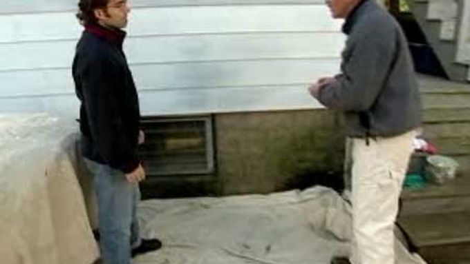 Two men standing on a paint tarp beside the aluminum siding of a house.