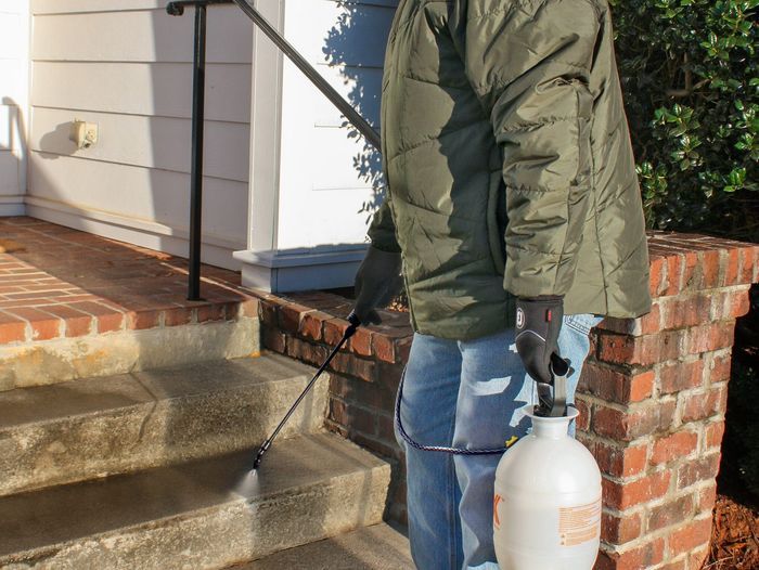 Photo of a man spraying a pet-safe ice prevention method on outdoor stairs