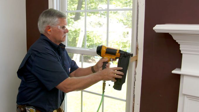 A man using a nailer to work on straightening a window.