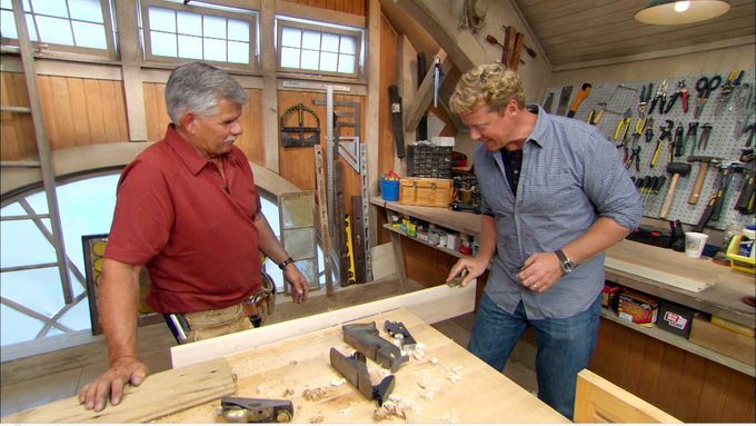 Two men looking at different hand plane options to use on a plank of wood.