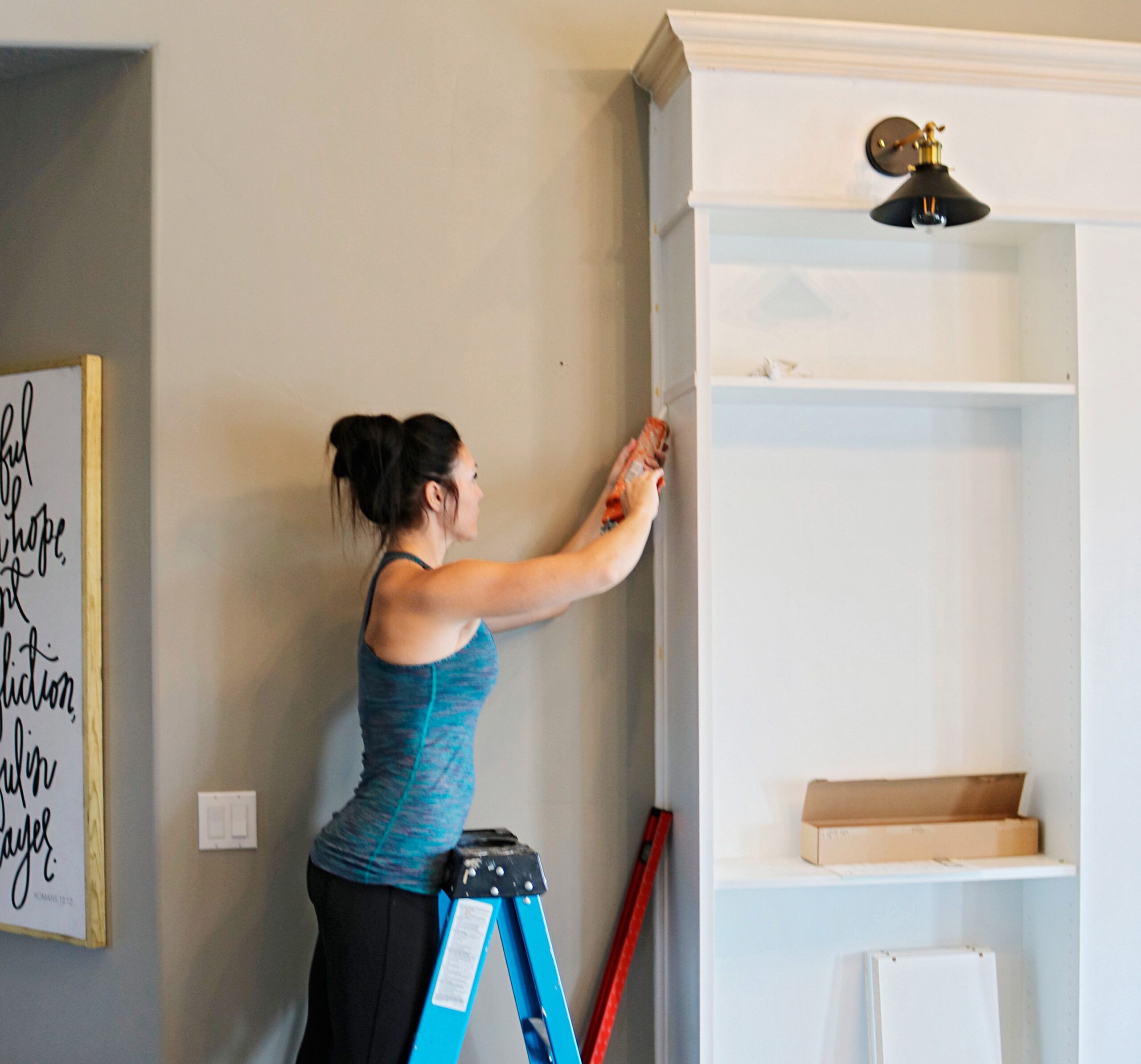 A person uses caulk on the outside of their built-in bookcase.