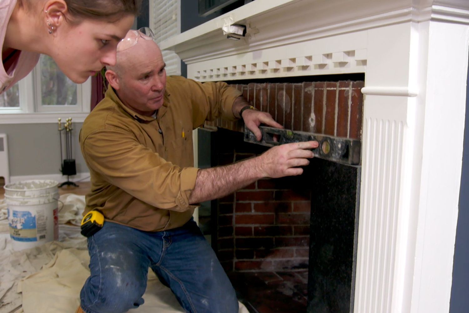 Two people applying tiling over a brick fireplace