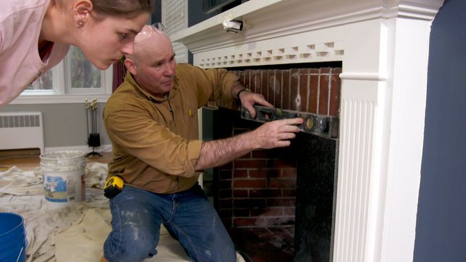 Two people applying tiling over a brick fireplace