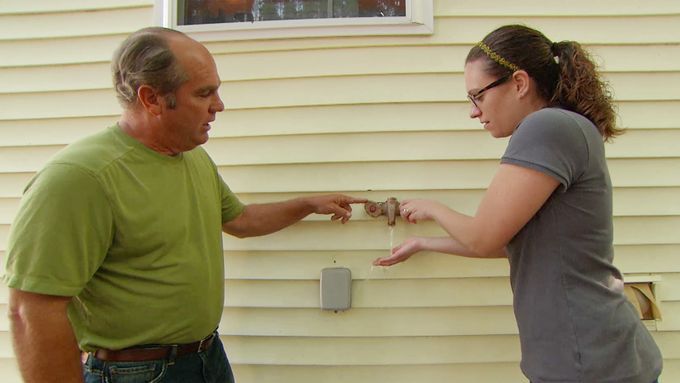 Two people using an outdoor faucet to get water.