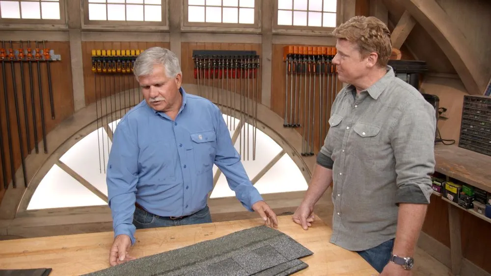 Two men in front of a table with roofing materials on top of it.