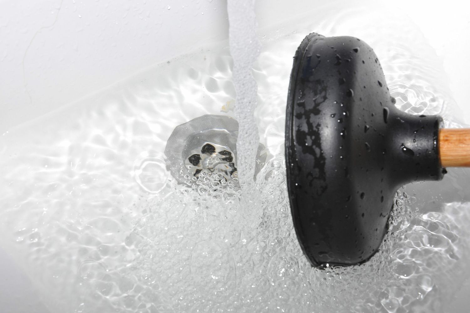 Faucet running to slow-draining tub drain and a plunger to ready to unclog the drain. Plunger_iStock_1133616931