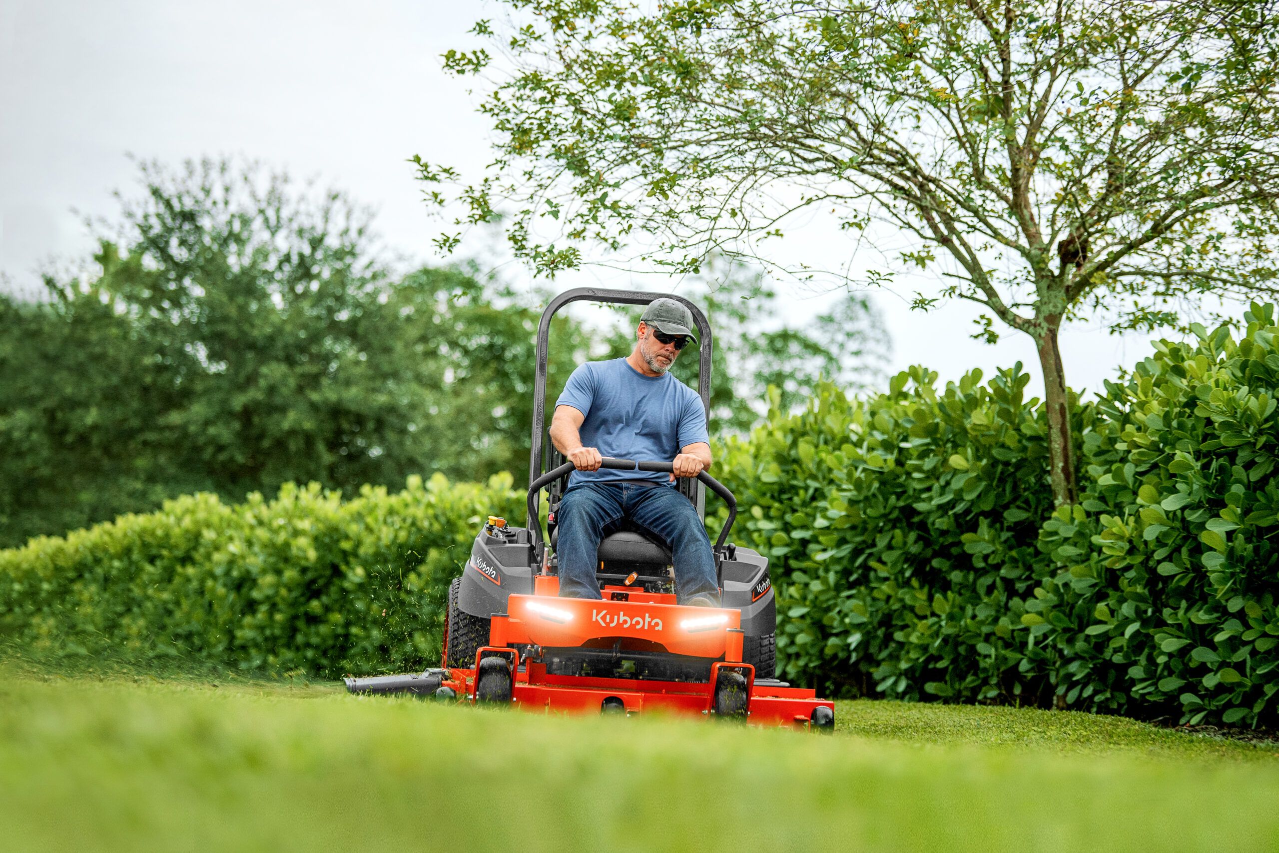 A man driving a zero-turn lawn mower across a lawn.