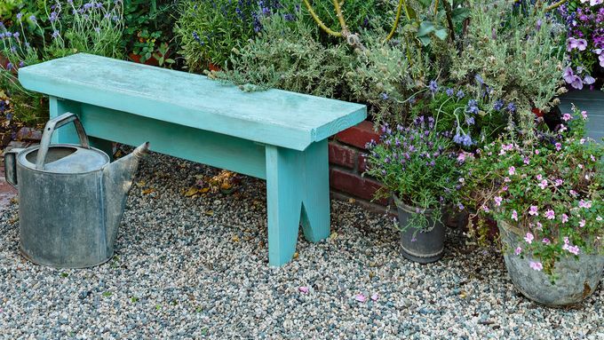 A blue garden bench in front of several potted plants.