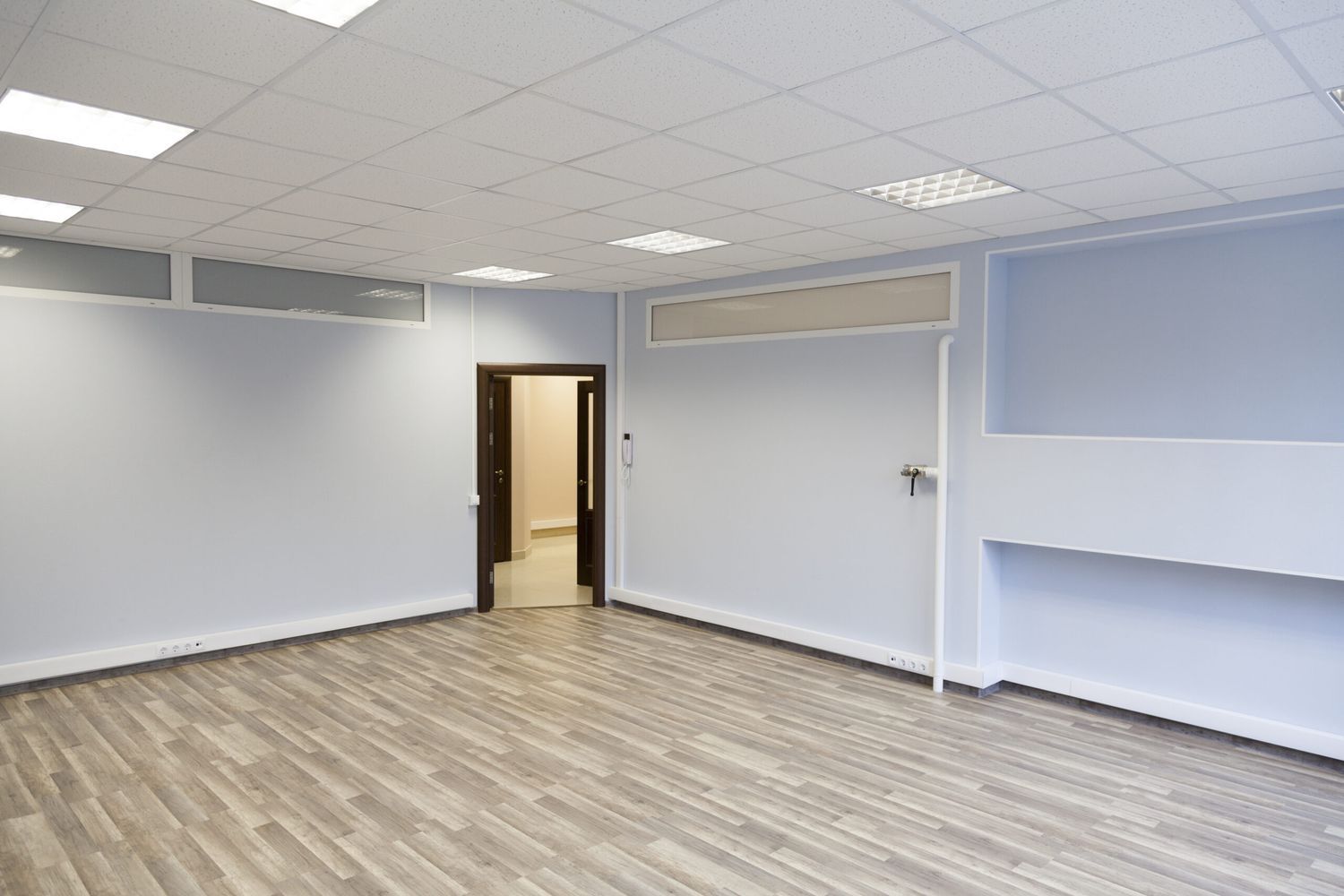 An empty room with an open door in the corner and a drop ceiling.
