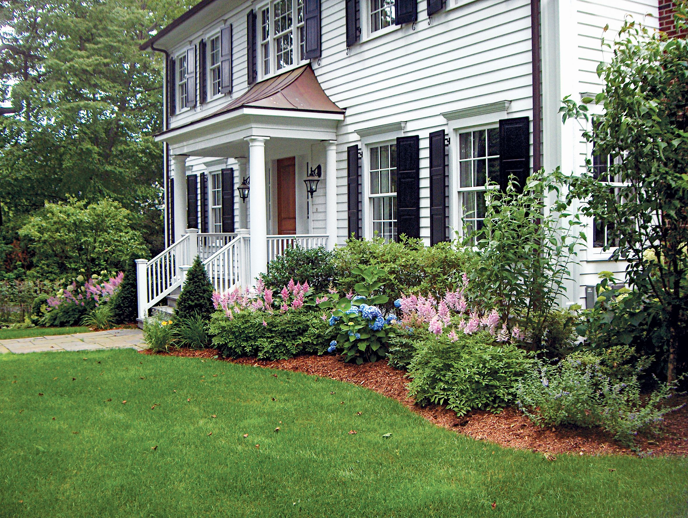 A white home surrounded by lush greenery and flowers. 