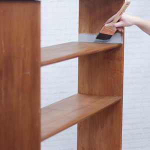 using a paintbrush and roller to prime an old bookcase