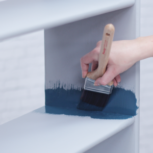 using a paintbrush and paint roller to paint an old bookcase