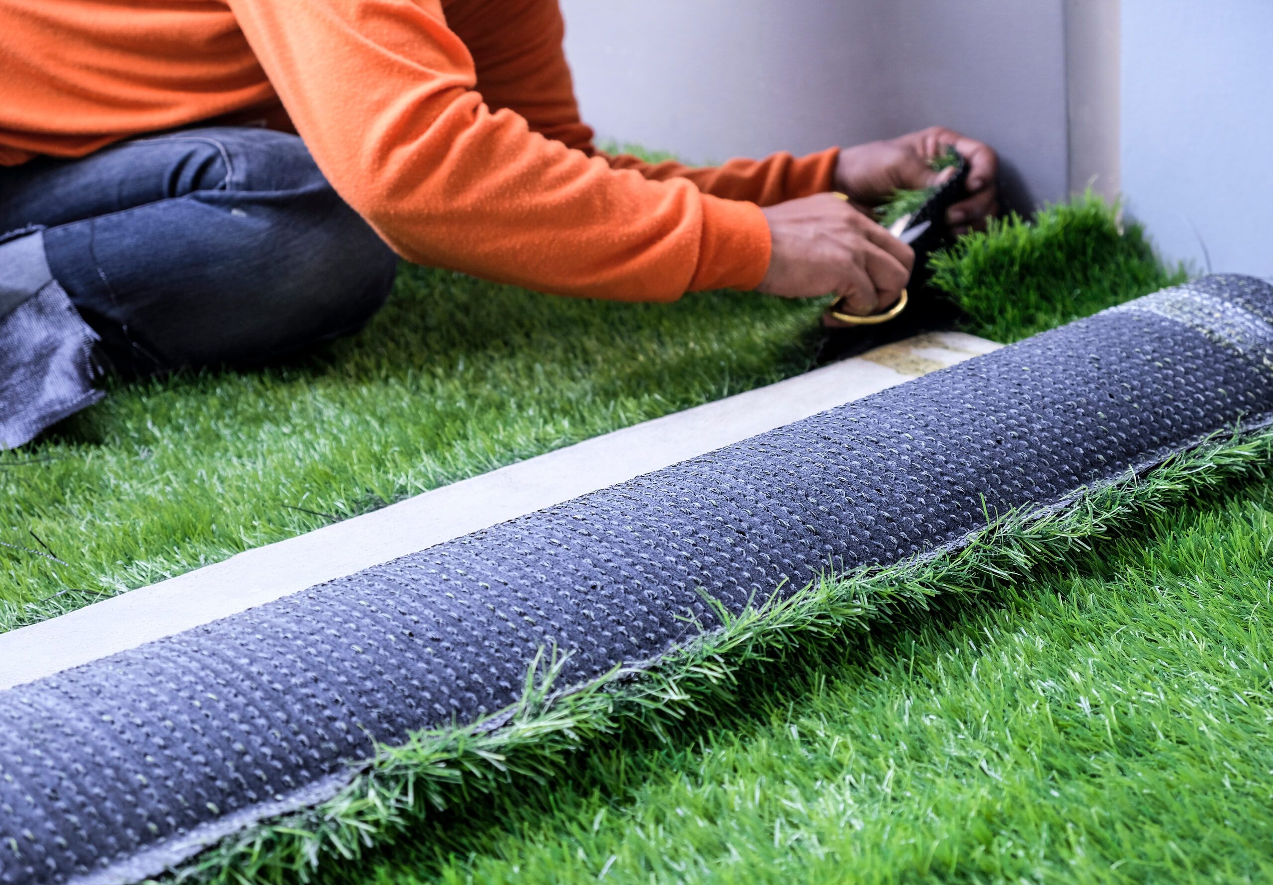 A man rolling artificial grass out onto a lawn.