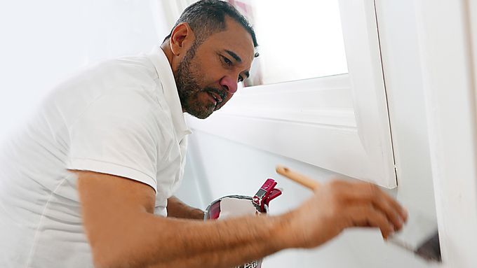 A man using a brush to paint varnished wood trim.