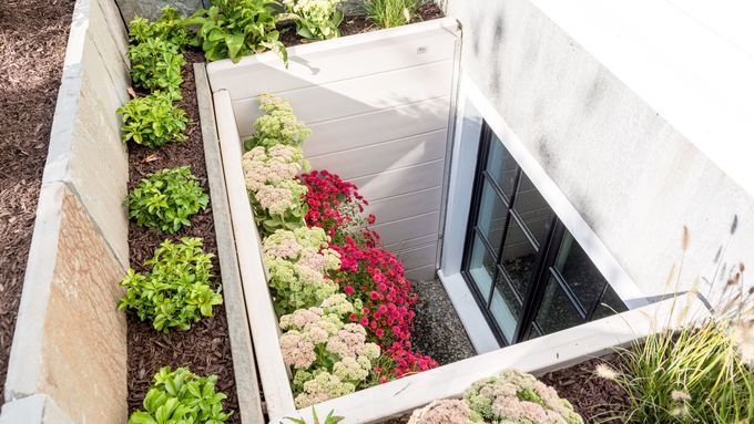 A closed egress window surrounded by plants and flowers.