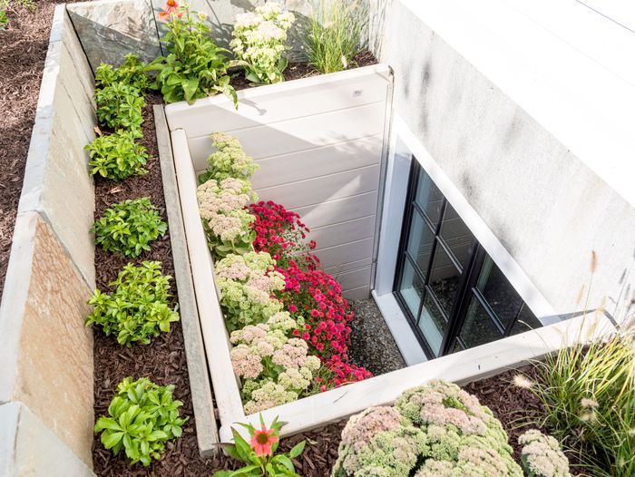 A closed egress window surrounded by plants and flowers.