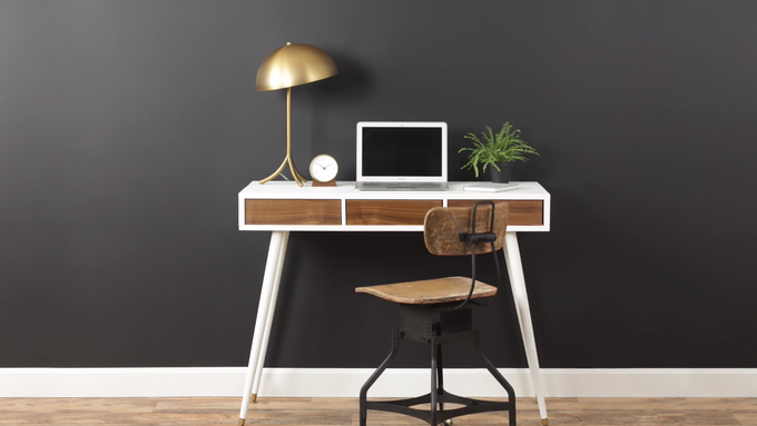 A computer desk in front of a wall that is painted black.